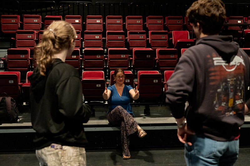 Two Theatre Arts students standing in the Flex Theatre, seen from behind, listening as their instructor explains a concept