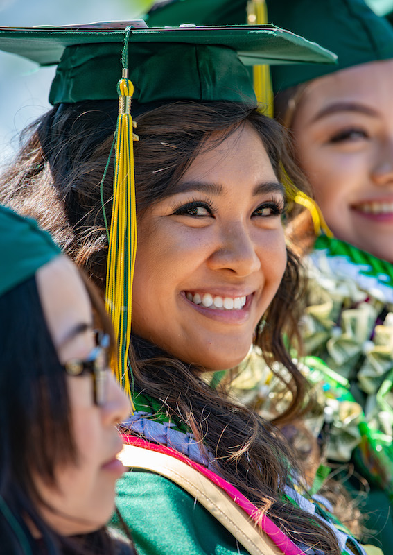 photo portrait of student wearing green cap and gown at the college commencement