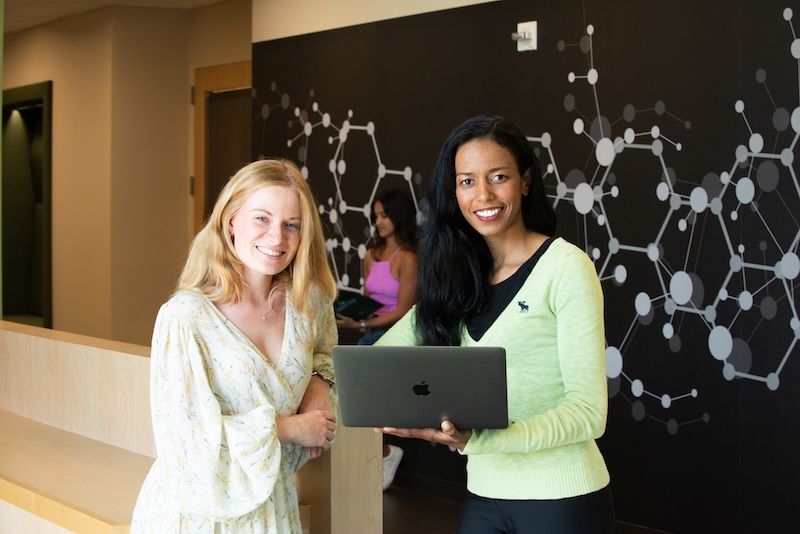 Peer mentor assisting a mentee while standing next to them and using a laptop.