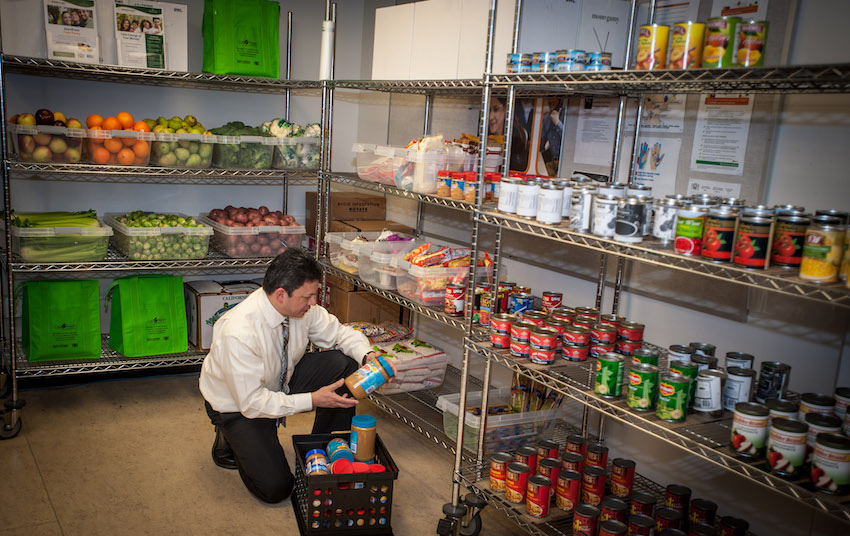 Person on one knee while holding a jar and restocking shelves in the campus food pantry