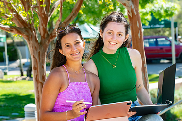 Two Cañada College students smiling outdoors while using a tablet and laptop